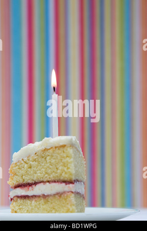 Tranche de gâteau d'anniversaire avec une bougie allumée contre un arrière-plan coloré à rayures pastel Banque D'Images