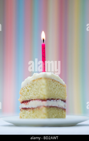 Tranche de gâteau d'anniversaire avec une bougie allumée contre un arrière-plan coloré à rayures pastel Banque D'Images