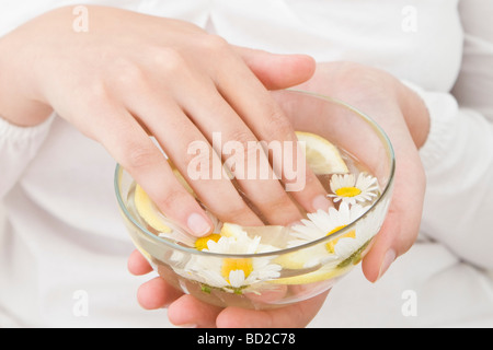 Femme mettant les mains dans le bol avec de l'eau, de citron et de camomille Banque D'Images