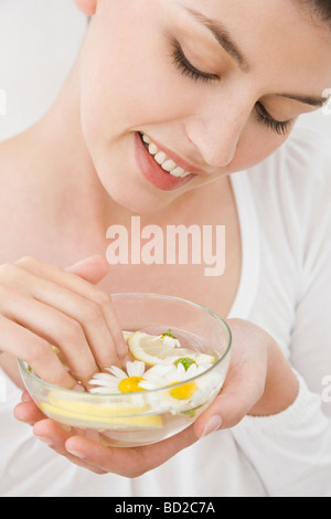 Femme mettant les mains dans le bol avec de l'eau, de citron et de camomille Banque D'Images