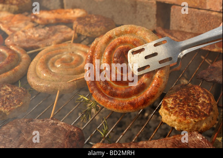 La viande barbecue charbon Smokey l'accent sur les grappins de tourner une spirale de saucisses de Cumberland Banque D'Images