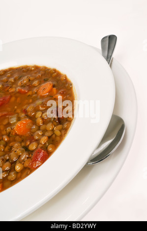 Bol de soupe de lentilles aux tomates et carrotwith une cuillère sur fond blanc. Banque D'Images