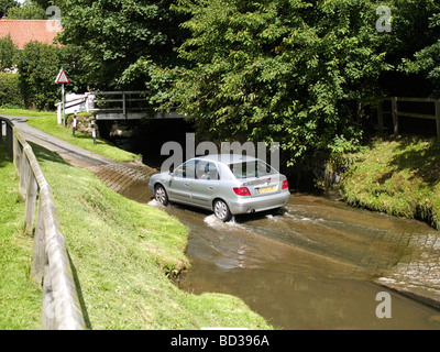 Un moteur voiture en traversant un gué sur un ruisseau sur une route de campagne dans un village du Yorkshire du Nord Banque D'Images