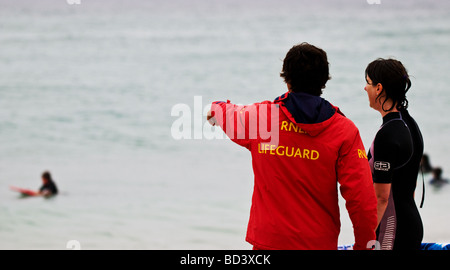 Un surfeur de parler à un sauveteur RNLI sur la plage de Sennen à Cornwall. Banque D'Images