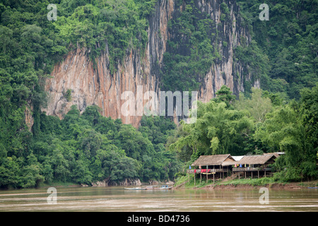 Falaises calcaires s'élèvent au-dessus de la rivière du Mékong comme les maisons s'asseoir sur la rive du fleuve sur pilotis, Luang Prabang, Laos 2006 Banque D'Images