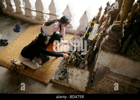 Les jeunes femmes allument des bougies à côté de statues de Bouddha dans les cavernes de calcaire de la grottes de Pak Ou sur le fleuve Mékong, Laos, 2006 Banque D'Images