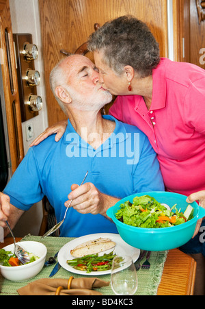 Man embrasse sa femme comme elle le sert le dîner dans leur motor home Banque D'Images