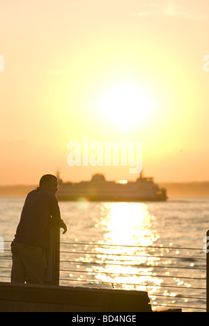 Un homme regarde le coucher du soleil à partir de la jetée à Alki Beach Park à Seattle, WA. Banque D'Images