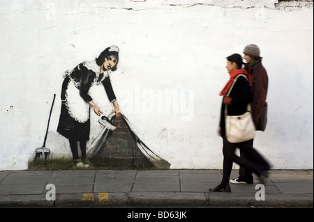 Deux piétons à pied passé du Banksy rues propres œuvres sur un mur sur Chalk Farm Road, London NW1, Décembre 2007 Banque D'Images