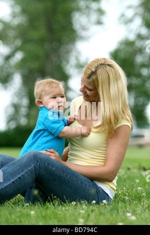 Smiling mother and baby son assise dans l'herbe. Banque D'Images