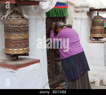 Bodhnath, au Népal. Adorateur bouddhiste priant à l'entrée du stupa. Roues de prière sur la gauche et la droite. Banque D'Images