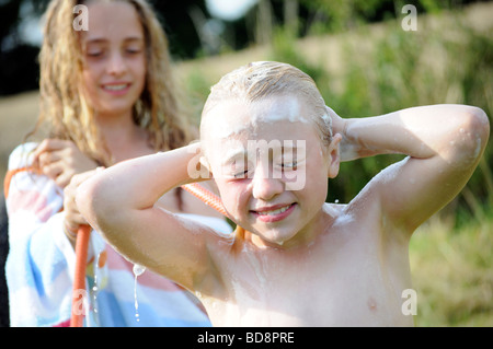 Photographie d'une jeune fille et laver avec de l'eau de refroidissement du tuyau flexible sur une journée d'été dans le jardin britannique UK Banque D'Images