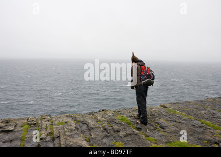 On Edge : une jeune femme se tient, les cheveux battant jusqu'au bord dun Angus. Howling winds blow a young woman's hair tout droit vers le haut Banque D'Images