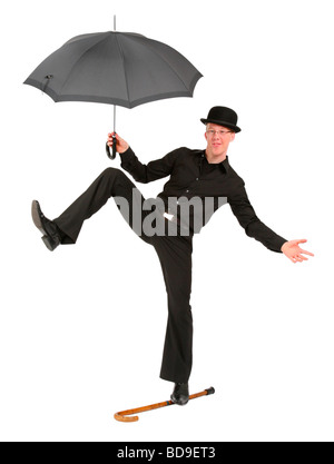 Jeune homme avec chapeau melon et parapluie en équilibre sur canne de marche Banque D'Images