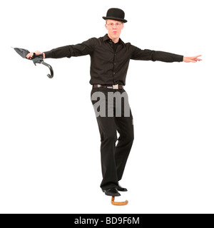 Jeune homme avec chapeau melon et parapluie en équilibre sur canne de marche Banque D'Images