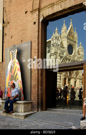 'Homme est assis à l'ombre à l'extérieur du musée de Santa Maria della Scala avec le Duomo (cathédrale) reflète dans la porte Banque D'Images