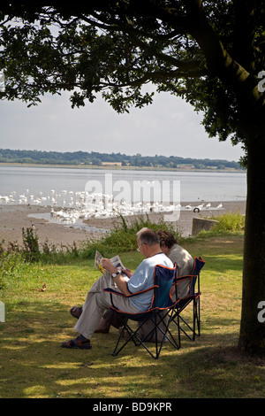 Deux personnes âgées, s'asseoir et lire à l'OMBRE À MANNINGTREE , BRITAINS PLUS PETITE VILLE SUR LA RIVIÈRE Stour, À CÔTÉ DE LA RIVIÈRE Banque D'Images