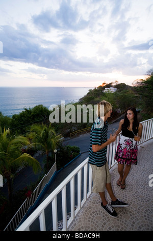 Un jeune couple parler ensemble et boire du vin alors que le soleil se couche derrière eux. Au Mar y Sol à Guanacaste, Costa Rica Banque D'Images