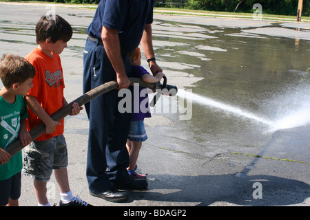 Les enfants en utilisant le tuyau d'incendie avec fireman Owosso City Fire Department d''Owosso MI USA Banque D'Images