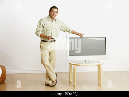 Mid adult man holding a permanent et à distance près d'un téléviseur Banque D'Images