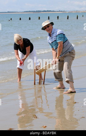 Homme et femme jouant au cricket au bord de la mer, couple à la retraite, profitant d'un exercice sain sur la plage. Bognor Regis, West Sussex, Royaume-Uni Banque D'Images