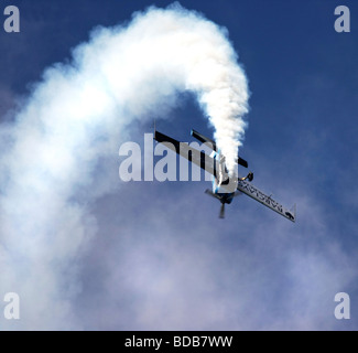 Avion de voltige bleu faisant une boucle la boucle rouleau et laissant une large traînée de fumée blanche derrière elle moelleux Banque D'Images