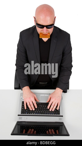 L'homme à la tête chauve avec des lunettes et une carte de crédit dans la bouche assis devant un ordinateur portable Banque D'Images