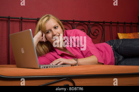 Girl lying on a bed with her laptop Banque D'Images