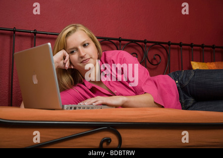 Girl lying on a bed with her laptop Banque D'Images