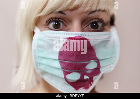 Une peur girl regarde dans l'appareil. Elle porte un masque chirurgical personnalisé avec un crâne rouge violet imprimé. Banque D'Images