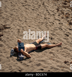 Jeune homme de soleil et lecture livre sur la plage aberystwyth Wales UK Banque D'Images
