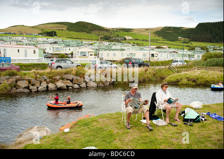 Les vacanciers lire les journaux assis par le flux à Clarach Bay holiday camp Ceredigion West Wales UK, dimanche matin Banque D'Images