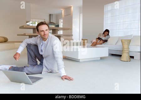Homme assis sur le sol avec sa femme lisant un livre à l'arrière-plan Banque D'Images