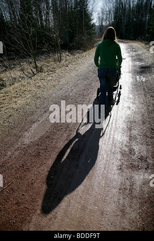 Une mère à son bébé dans un landau à travers une forêt en silhouette dans le soleil d'hiver froid faible. Parution du modèle Banque D'Images