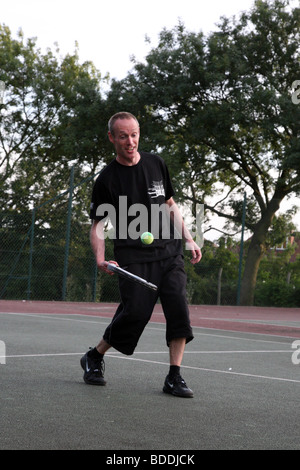Homme d'environ 40 ans à jouer au tennis dans son parc local Banque D'Images