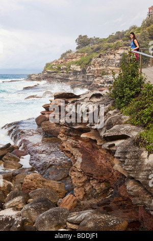 Une femme debout sur la côte de Sydney le long de la promenade côtière de la plage de Bondi Banque D'Images