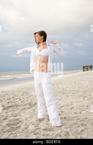 Young woman in white bikini top et pantalon beach stretching Banque D'Images