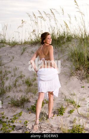 Young woman in white bikini top et jupe marche dans les dunes de sable de plage Banque D'Images