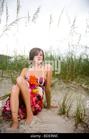 Jeune femme en robe d'été assis dans les dunes de sable sur la plage Banque D'Images