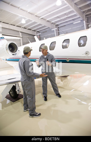 Deux mécaniciens avion having argument dans le hangar à côté de jet privé Banque D'Images