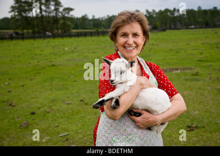 Senior woman holding baby goat sur le terrain Banque D'Images