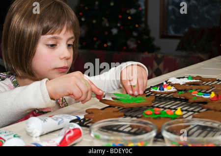 Une mignonne petite fille décore gingerbread cookies. Banque D'Images