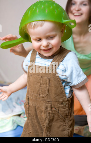 Mère a mis dans une passoire sur la tête de son petit sourire petite un ans, drôle de jeu Banque D'Images