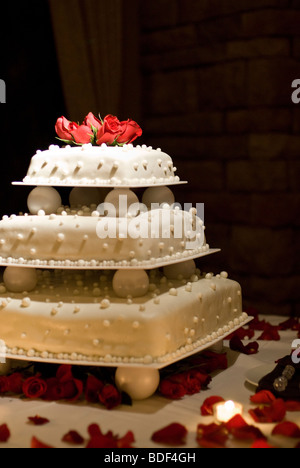 Un gâteau de mariage avec des roses rouges sur le dessus. Banque D'Images