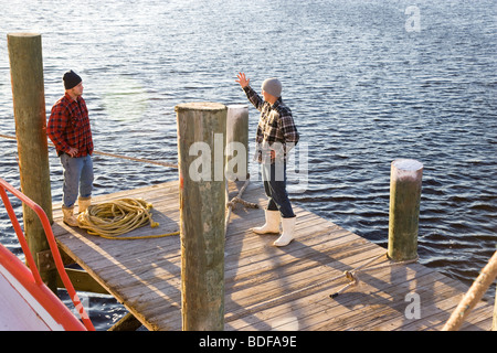 Les jeunes pêcheurs en chemises à carreaux debout sur le quai avec bateau de pêche près de la corde Banque D'Images