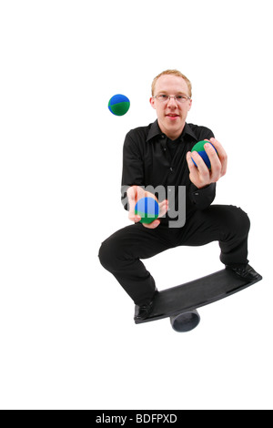 Jeune homme jonglant avec des balles et en équilibre sur un rola bola balance board Banque D'Images