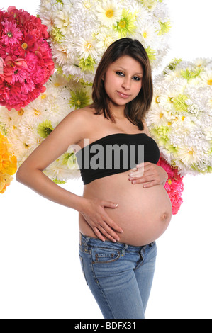 Pregnant Hispanic woman avec les mains sur le ventre avec des fleurs en arrière-plan Banque D'Images