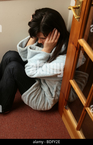 Jeune femme aux cheveux noirs assis dans un coin d'une pièce à la recherche appuyée ou peur. Banque D'Images