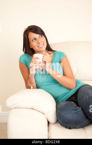 Jolie jeune fille souriant en pleine réflexion smiling sitting on a sofa Banque D'Images