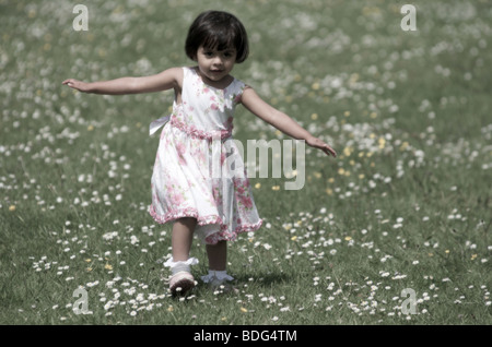 Une petite fille s'exécutant dans une prairie au printemps en couleurs pastel et soft focus Banque D'Images